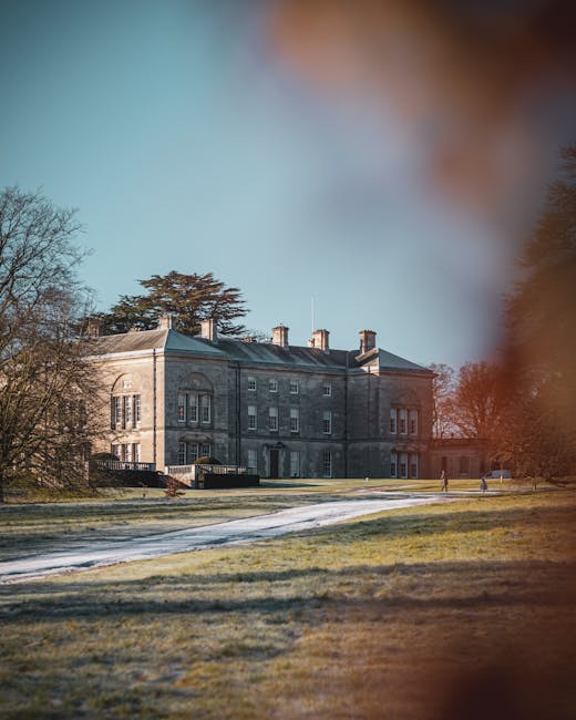 A large, historic stone mansion situated on a well-maintained lawn with pathways, surrounded by mature trees with bare branches, under a partly cloudy sky. The building features multiple chimneys, tall rectangular windows, and a symmetrical facade, indicative of traditional architectural style. In the foreground, the grassy area appears to be lightly frosted or damp, with a clear walking path leading toward the entrance. The scene is illuminated by soft natural light, creating a calm and pristine atmosphere, reflecting the importance of cleanliness and maintenance in residential settings. As part of cleaning practices for homes on Morden Hall Park Estate, tasks may include surface cleaning of exterior stonework, window washing, and turf maintenance, which [COMPANY_NAME] provides to ensure the property's aesthetic and hygiene standards are upheld. This image emphasizes the significance of thorough exterior and grounds cleaning as part of maintaining a beautiful, hygienic home environment, aligned to the themes of surface cleaning, deep cleaning, and sanitisation discussed on the webpage.